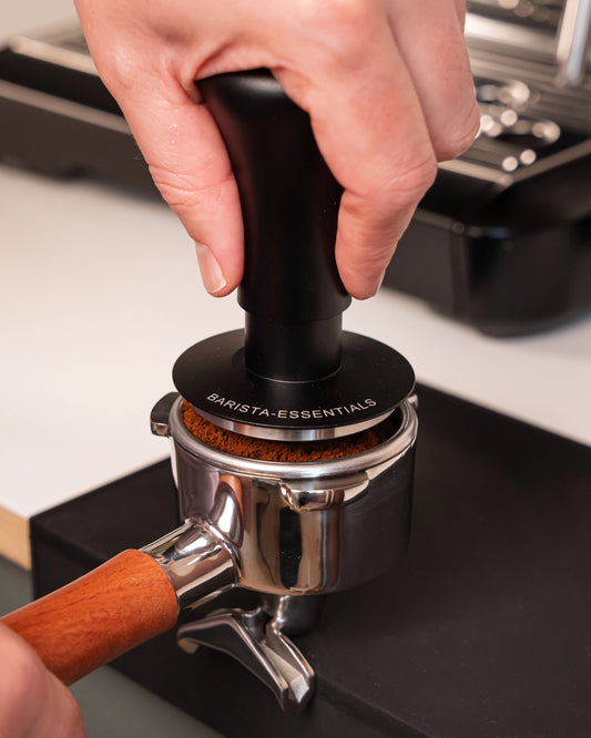 Hand drukt een zwarte 53,3 mm klik-tamper in een filterdrager
