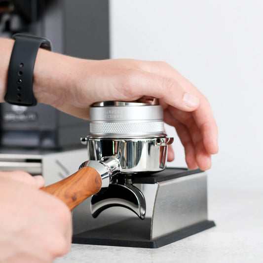 Hand drukt met een tamper koffie aan in een portafilter op het zilveren station