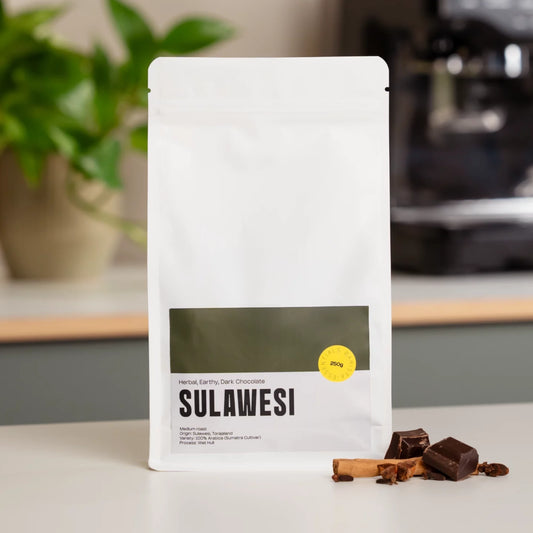 Zakje Sulawesi Indonesië koffie met een espressomachine op de achtergrond.