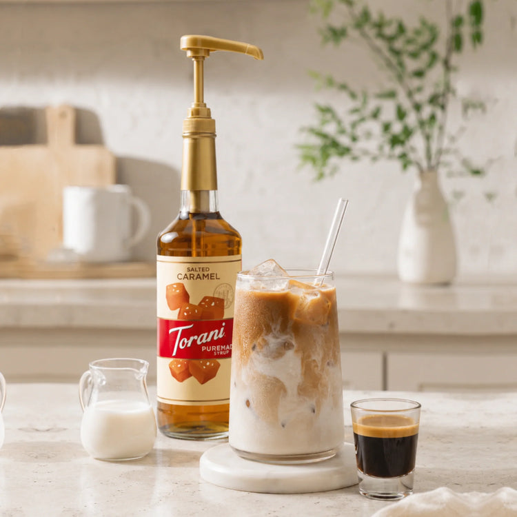 Glas iced coffee met espresso, melk, ijsblokjes en Torani koffiesiroop op een thuisbarista koffiestation