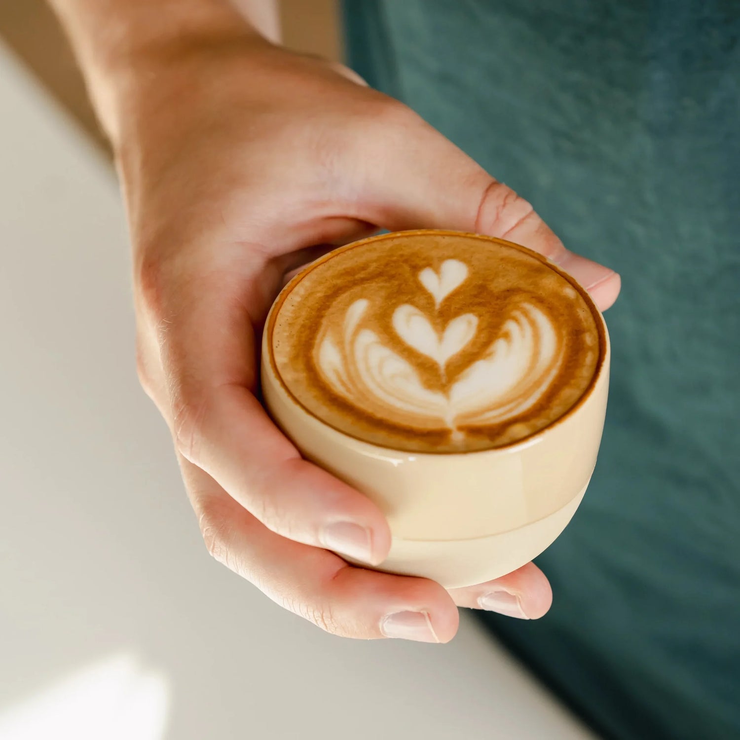 Zandgeel cappuccino kopje van keramiek met latte art, vastgehouden door barista. Ideaal voor thuisgebruik met populaire espressomachines en melkopschuimers.