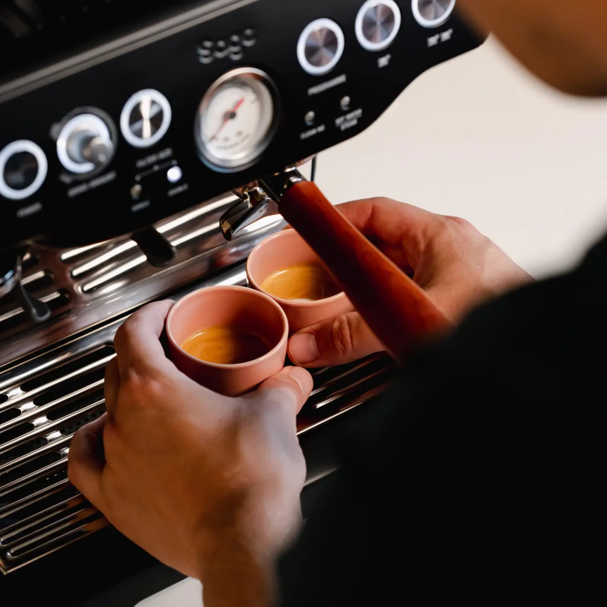 Thuisbarista plaatst roze espressokopjes van 60 ml onder pistonmachine van Philips, Gaggia of Krups. Deze handgemaakte kopjes zijn stapelbaar, beschermen de cremalaag en passen perfect bij machines met stoompijpje.