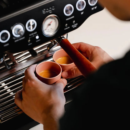 Thuisbarista plaatst roze espressokopjes van 60 ml onder pistonmachine van Philips, Gaggia of Krups. Deze handgemaakte kopjes zijn stapelbaar, beschermen de cremalaag en passen perfect bij machines met stoompijpje.