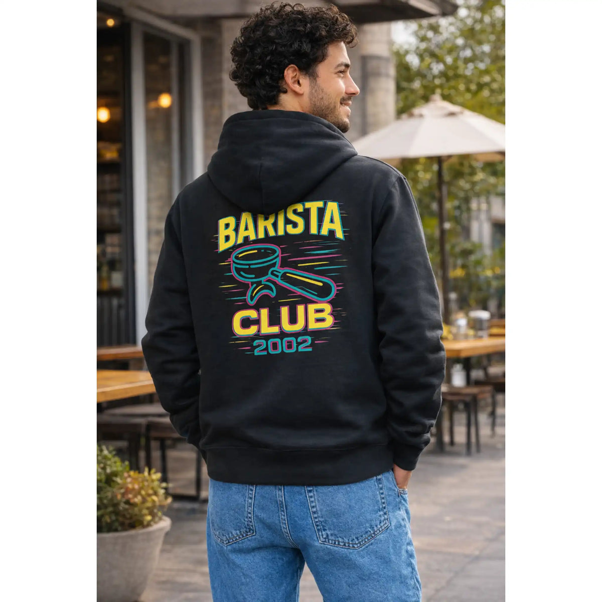 Zwarte barista hoodie met kleurrijk Barista Club koffie ontwerp op de rug, gedragen door een barista in stedelijke omgeving