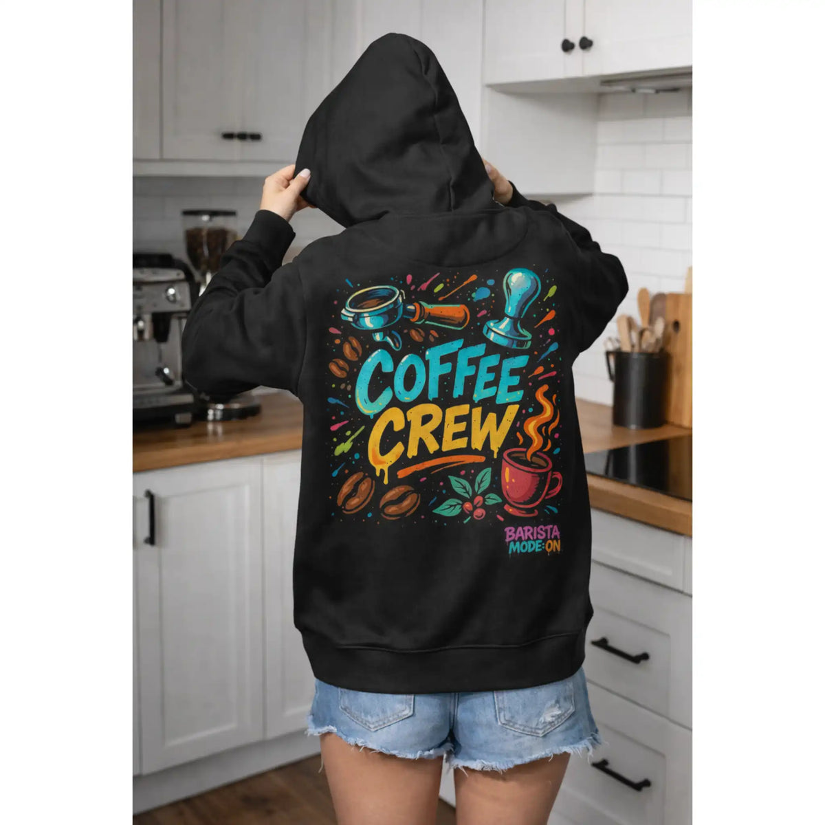 Zwarte barista hoodie met Coffee Crew ontwerp en koffie tools op de rug, gedragen in een keuken door een koffieliefhebber