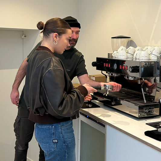 Barista-instructeur geeft uitleg aan een deelneemster bij de espressomachine tijdens de latte art workshop.