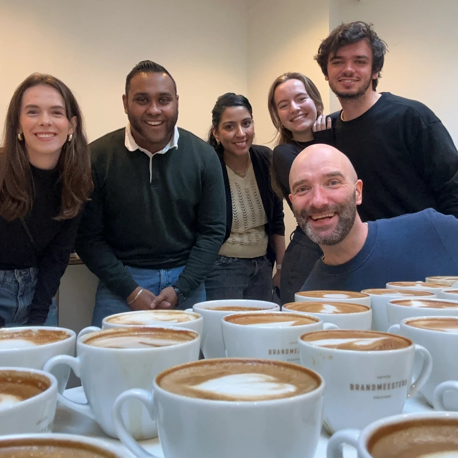 Geert-Jan de Baristaman met deelnemers na een barista workshop in Amsterdam, met cappuccino’s op de voorgrond.