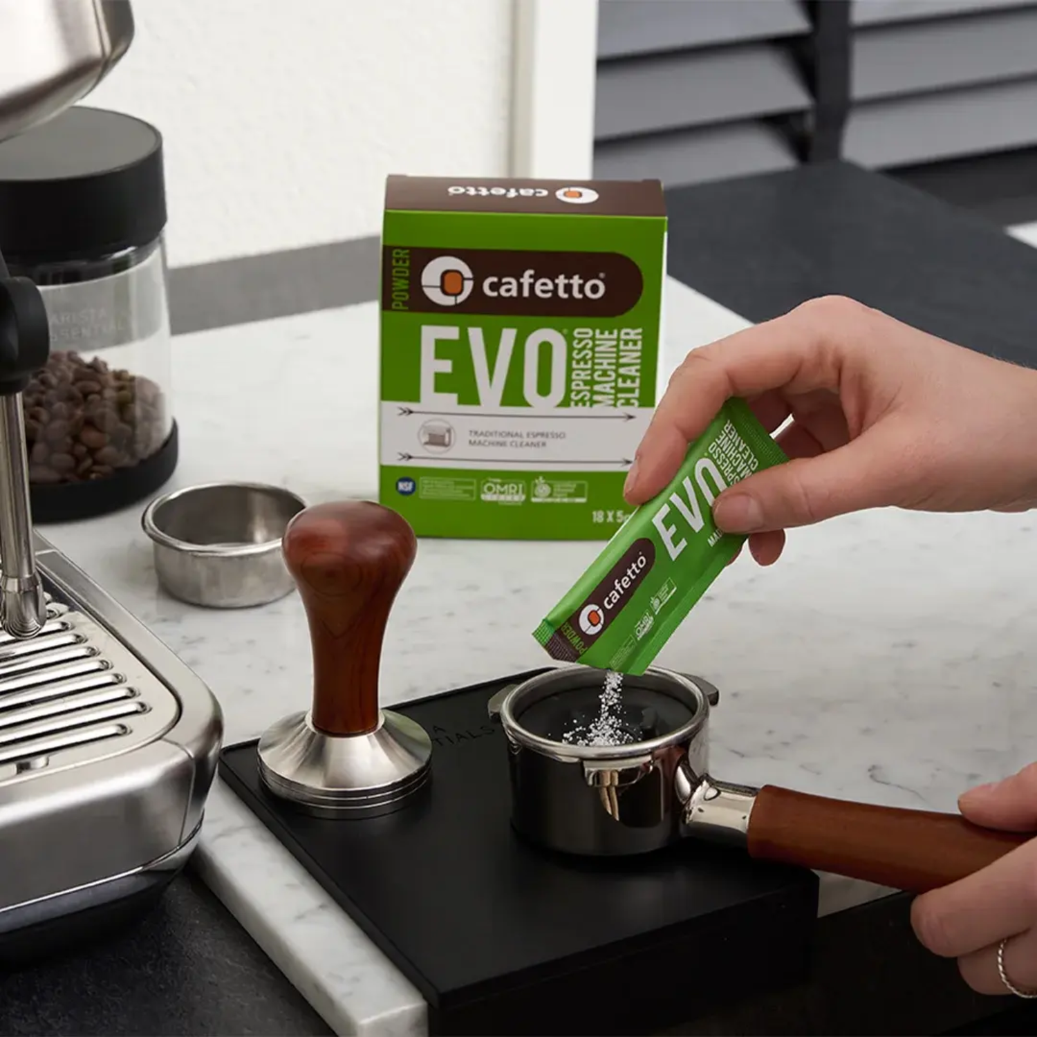 Hand giet Cafetto EVO blindfilterpoeder in portafilter om espressomachine zetgroep te reinigen.