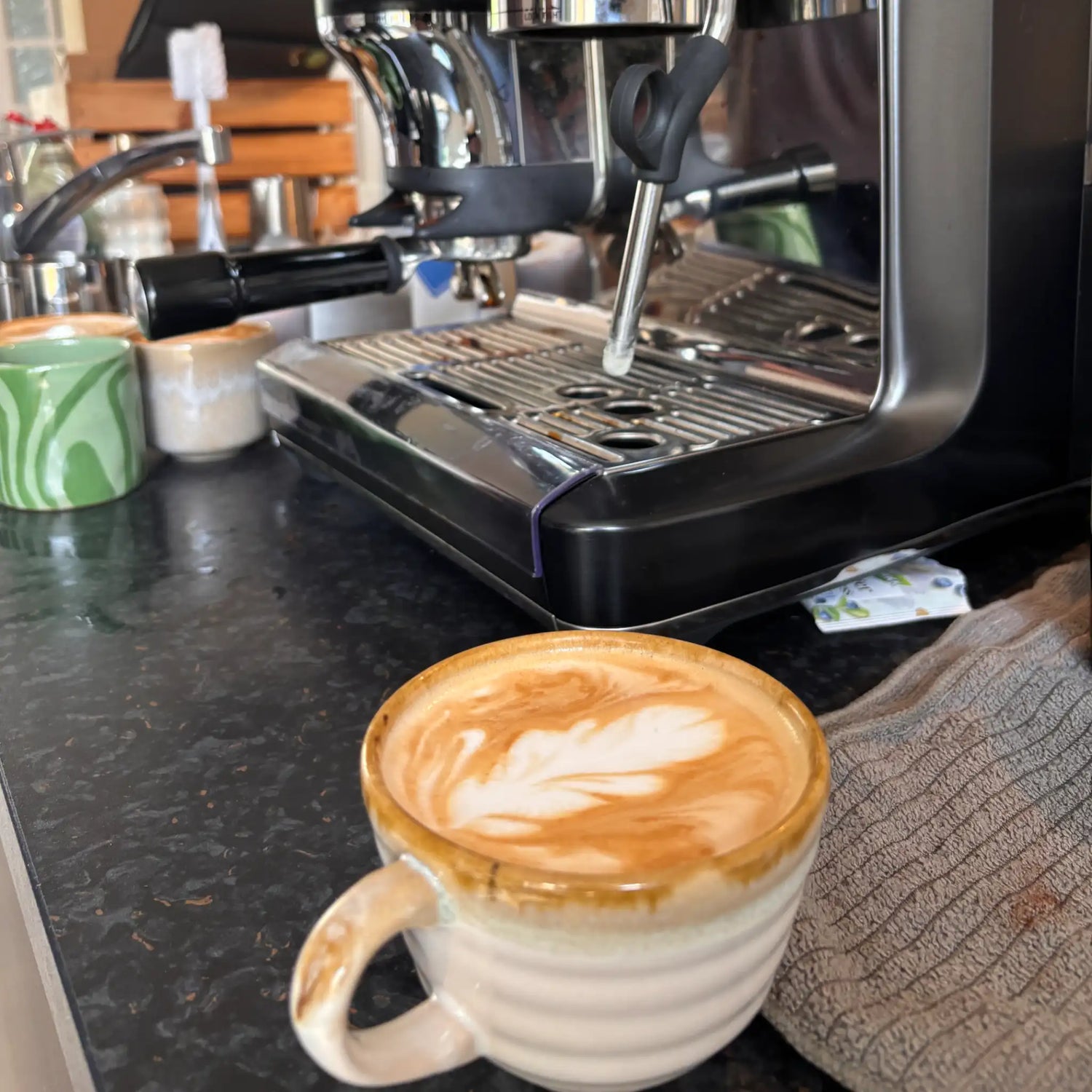 Cappuccino met latte art naast een Sage Barista Express Impress na oefenen met melk opschuimen tijdens een barista-workshop aan huis