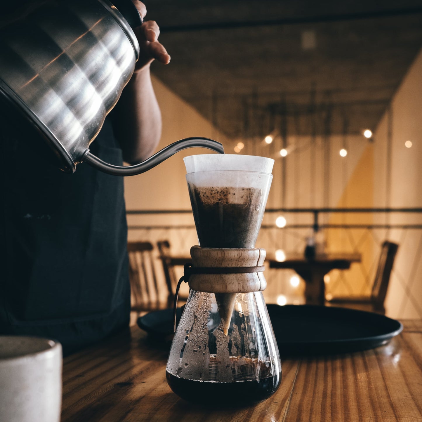 Chemex 3 Kops Koffiefilter in een Chemex 3 kops filtermethode. Sfeerbeeld van barista die met een waterketel water in de chemex met papieren filter giet. Afbeelding zijaanzicht.