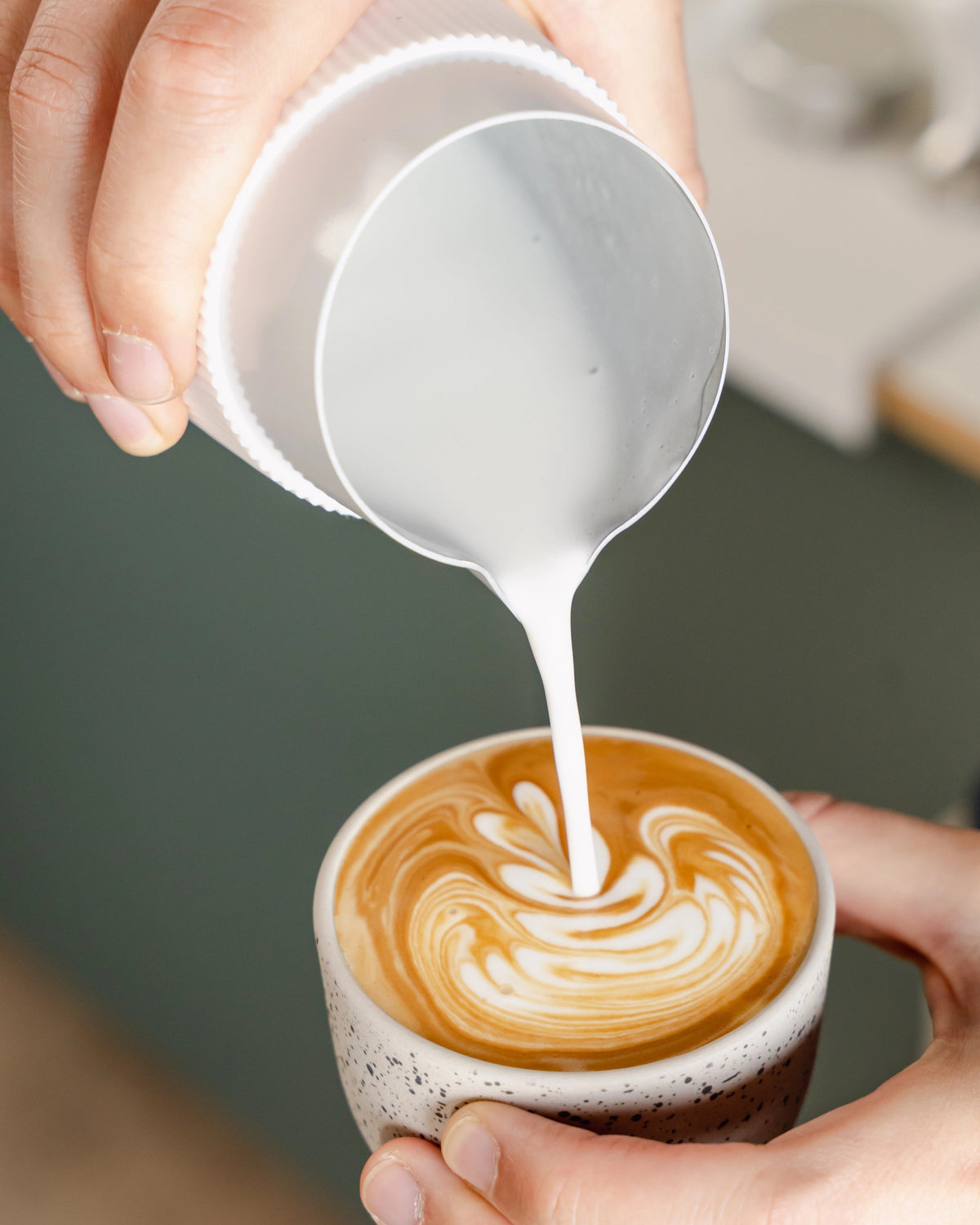 Melk uit een witte handvatloze kan in een cappuccino schenken