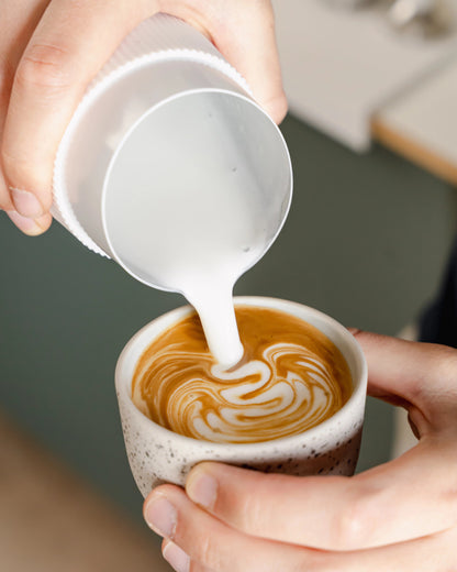 Latte art schenken met een witte handvatloze melkkan