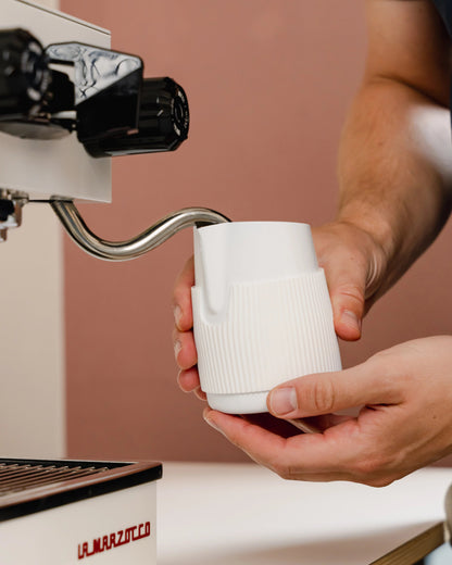 Witte handvatloze melkkan onder de stoompijp van een espressomachine