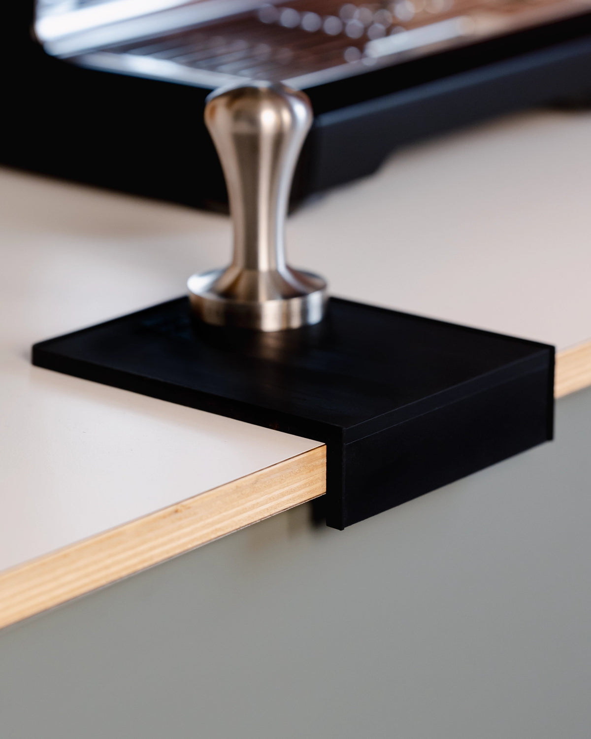 Een tamper op de kleine zwarte tampermat met hoek naast de espressomachine