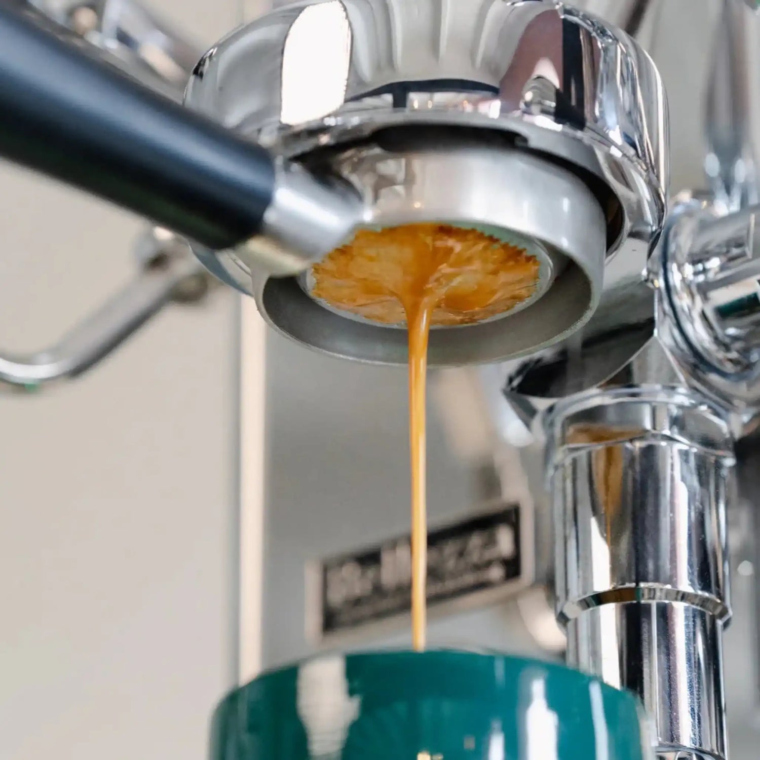 Dubbel filterbakje in naked portafilter tijdens espresso extractie met 9 bar druk, voorbeeld van gelijkmatige extractie voor het correct afstellen van je koffiemaler