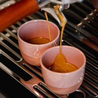 Twee roze porseleinen espressokopjes (60 ml) vullen zich met espresso onder een stoompijpje-machine van Sage of De’Longhi. Ontworpen voor thuisbarista’s die het beste uit hun cremalaag willen halen, in stijlvol en stevig roze porselein.