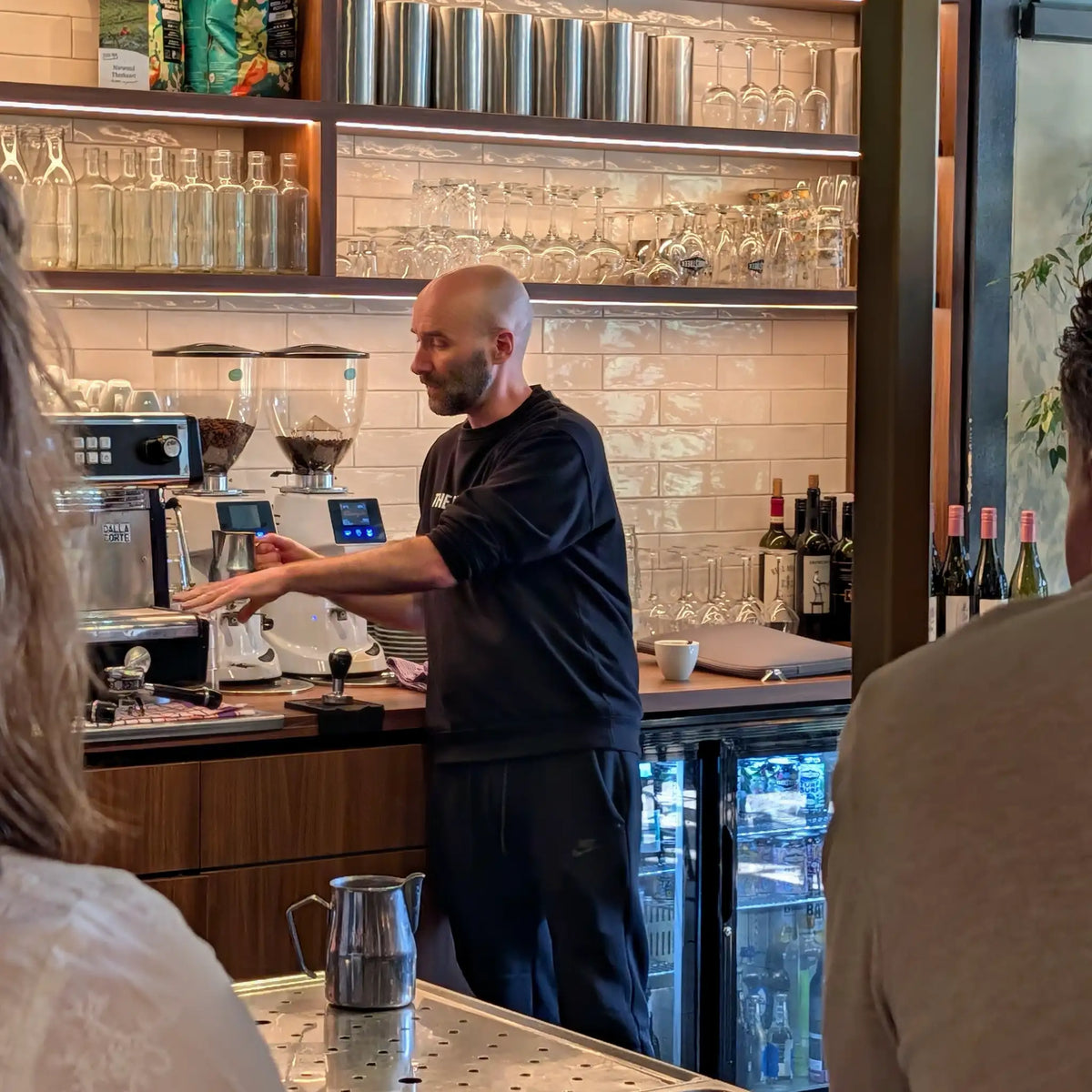 Geert-Jan de Baristaman geeft uitleg over de professionele espressomachine tijdens een zakelijke barista workshop, terwijl deelnemers luisteren.