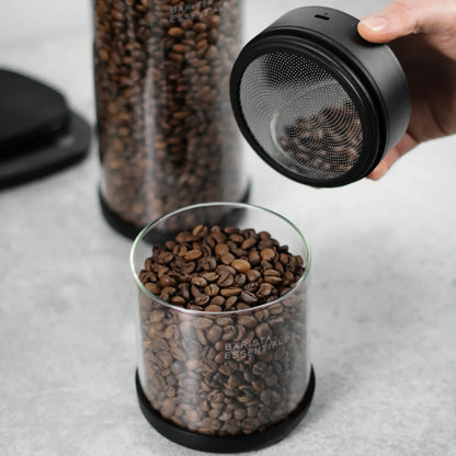 Hand tilt de zwarte deksel van een glazen koffiebus met bonen