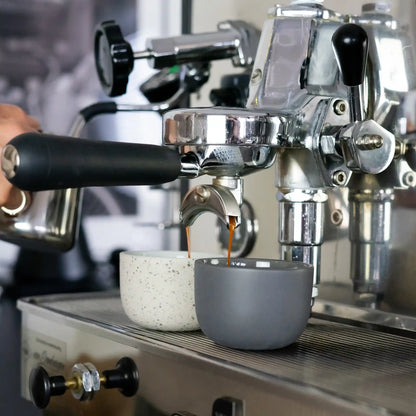 Grijs en gestippeld kopje onder de uitloop van een espressomachine