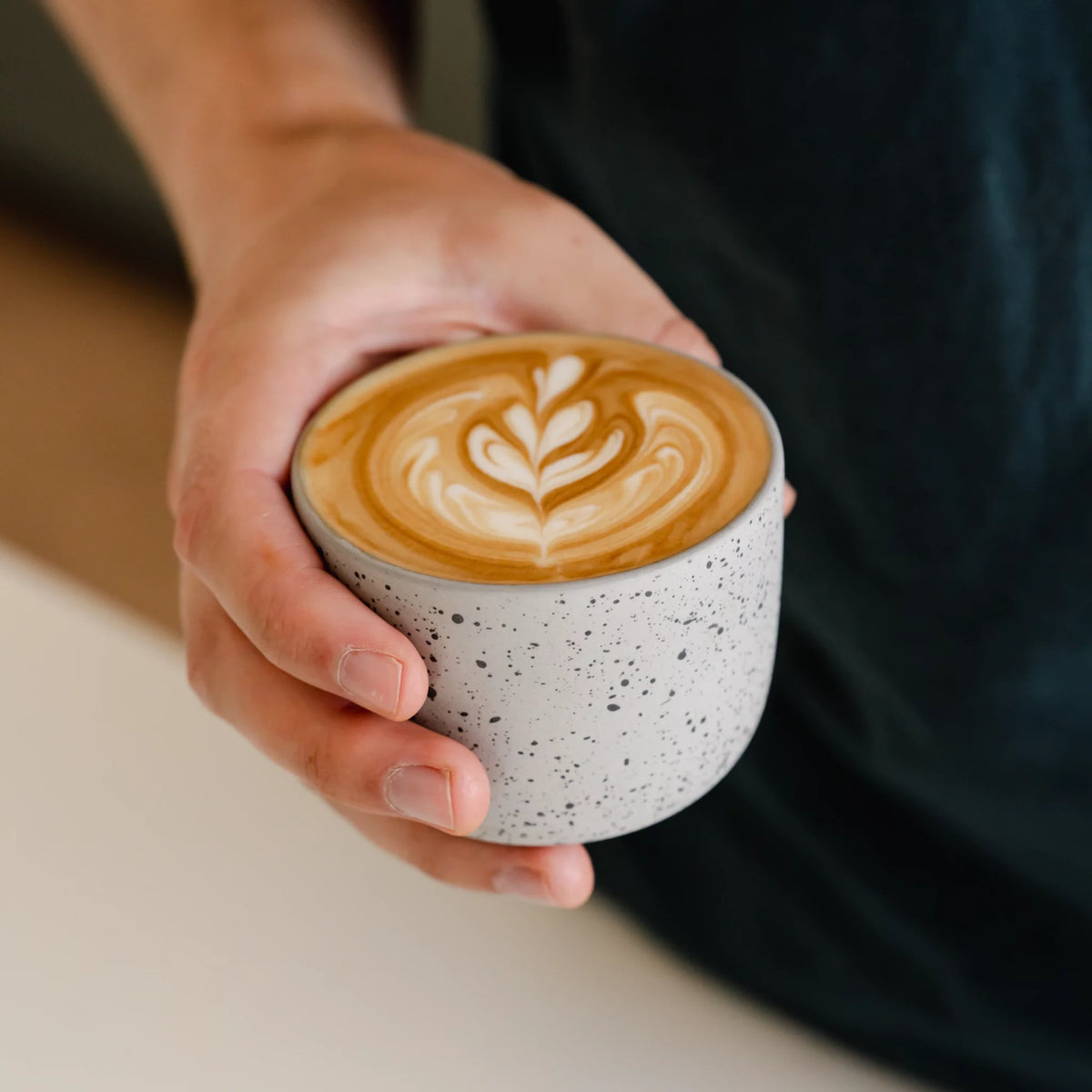 Hand houdt een gestippeld kopje met latte art