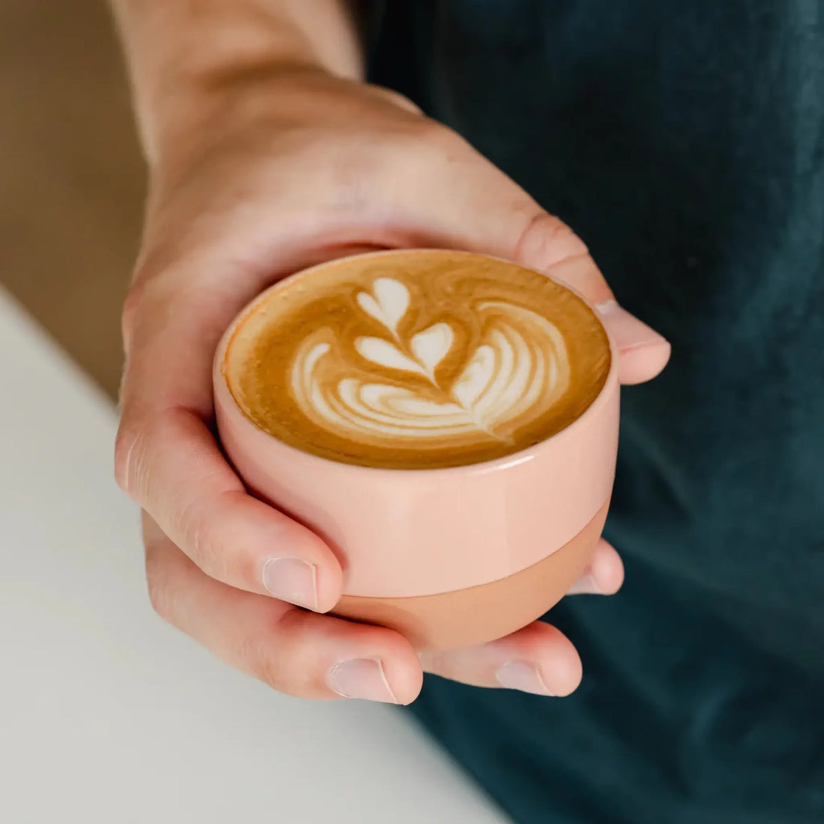 Hand houdt een roze kopje met latte art