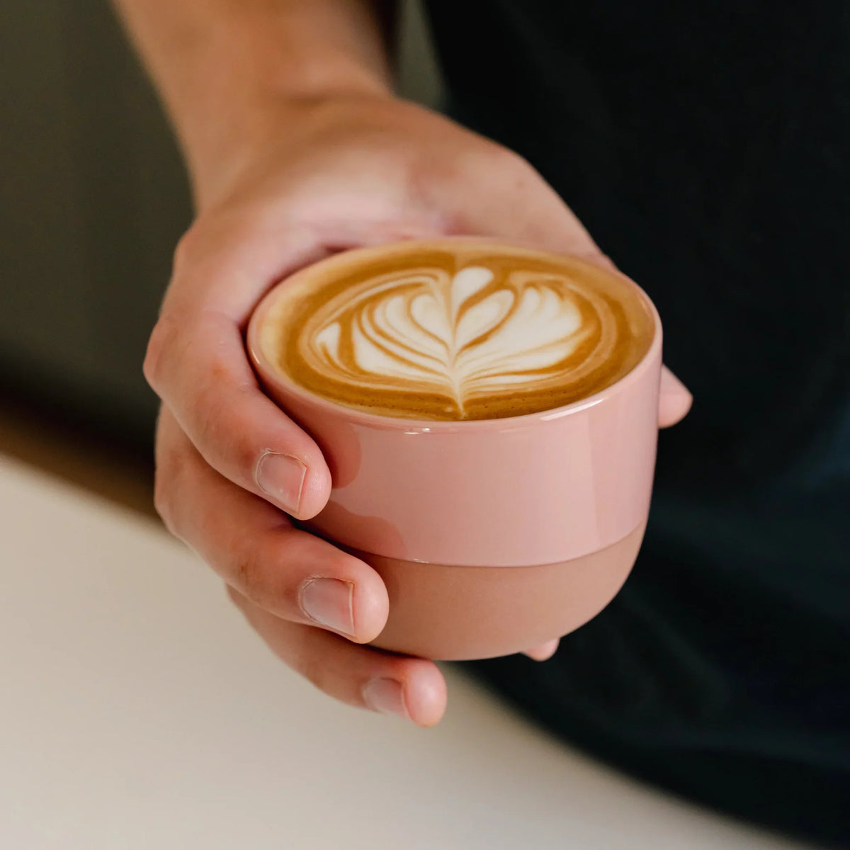 Hand houdt een roze kopje met latte art