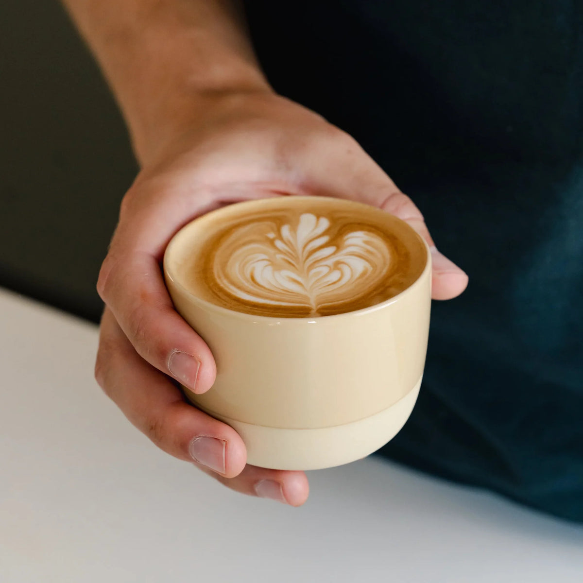Hand houdt een zandgeel kopje met latte art