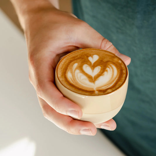 Hand houdt een zandgeel kopje met latte art