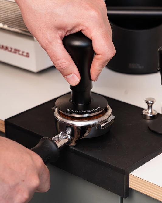 Hand drukt een zwarte 58,5 mm klik-tamper in een filterdrager