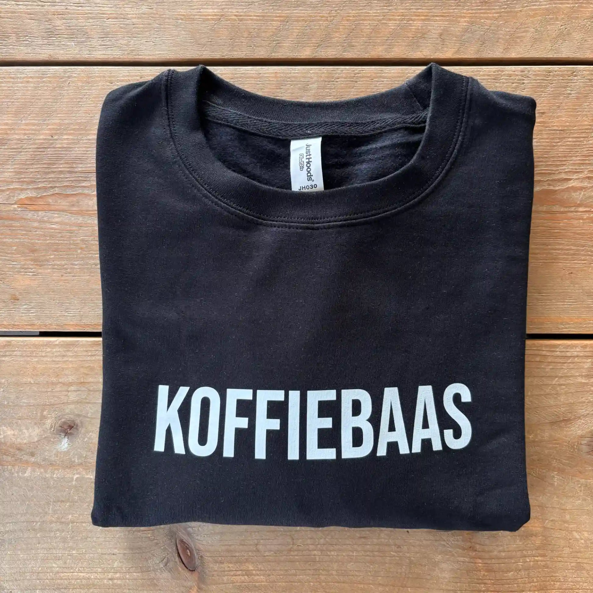 Zwart “KOFFIEBAAS” sweatshirt netjes opgevouwen – perfect koffiecadeau voor barista’s
