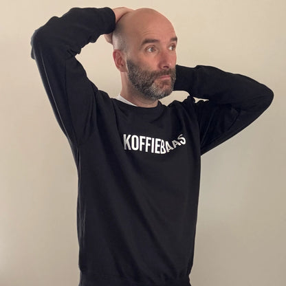 Casual sfeerbeeld van man met zwarte “KOFFIEBAAS” sweater – barista stijl