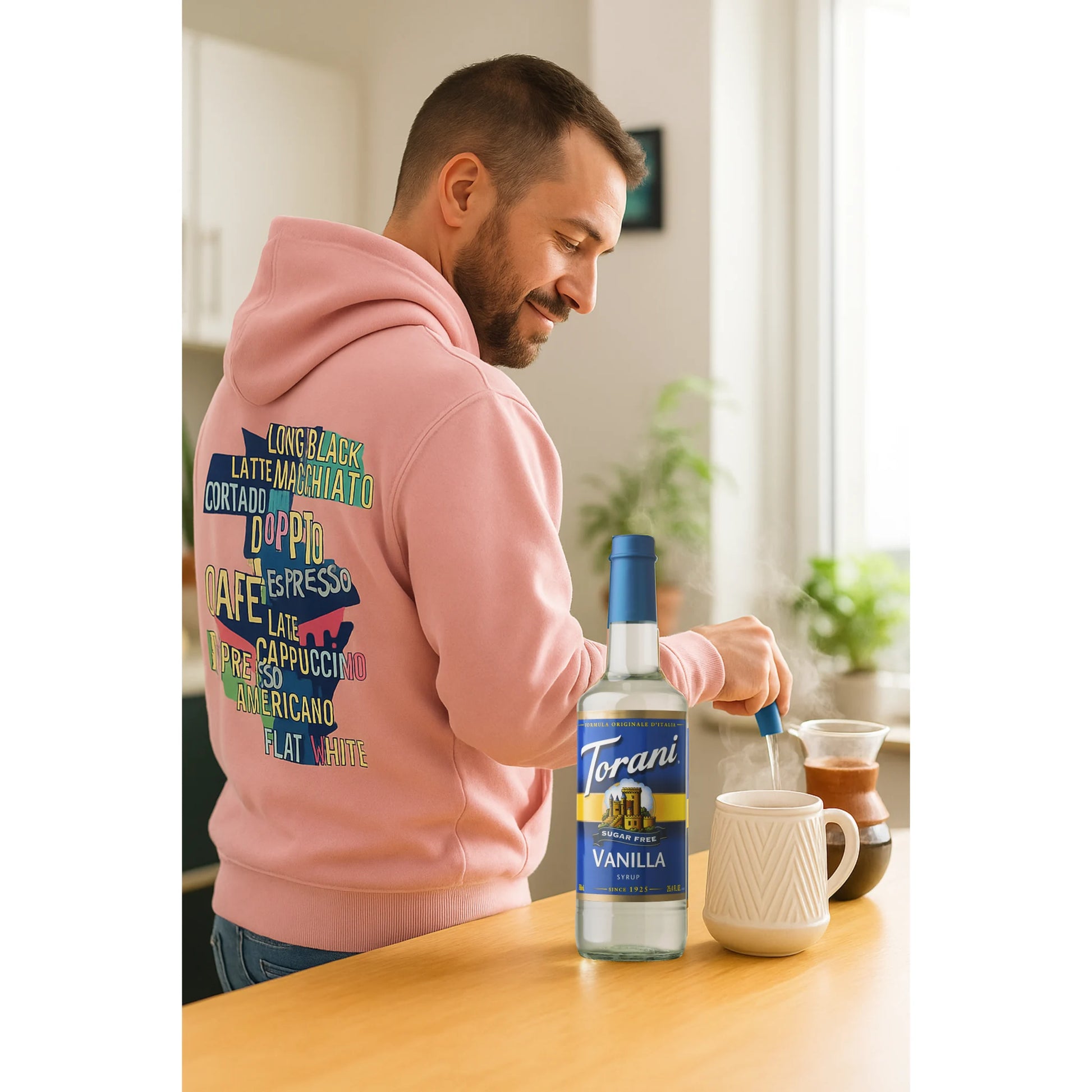 Man maakt koffie met Torani suikervrije vanillesiroop in barista hoodie – een origineel en gezond cadeau voor koffieliefhebbers