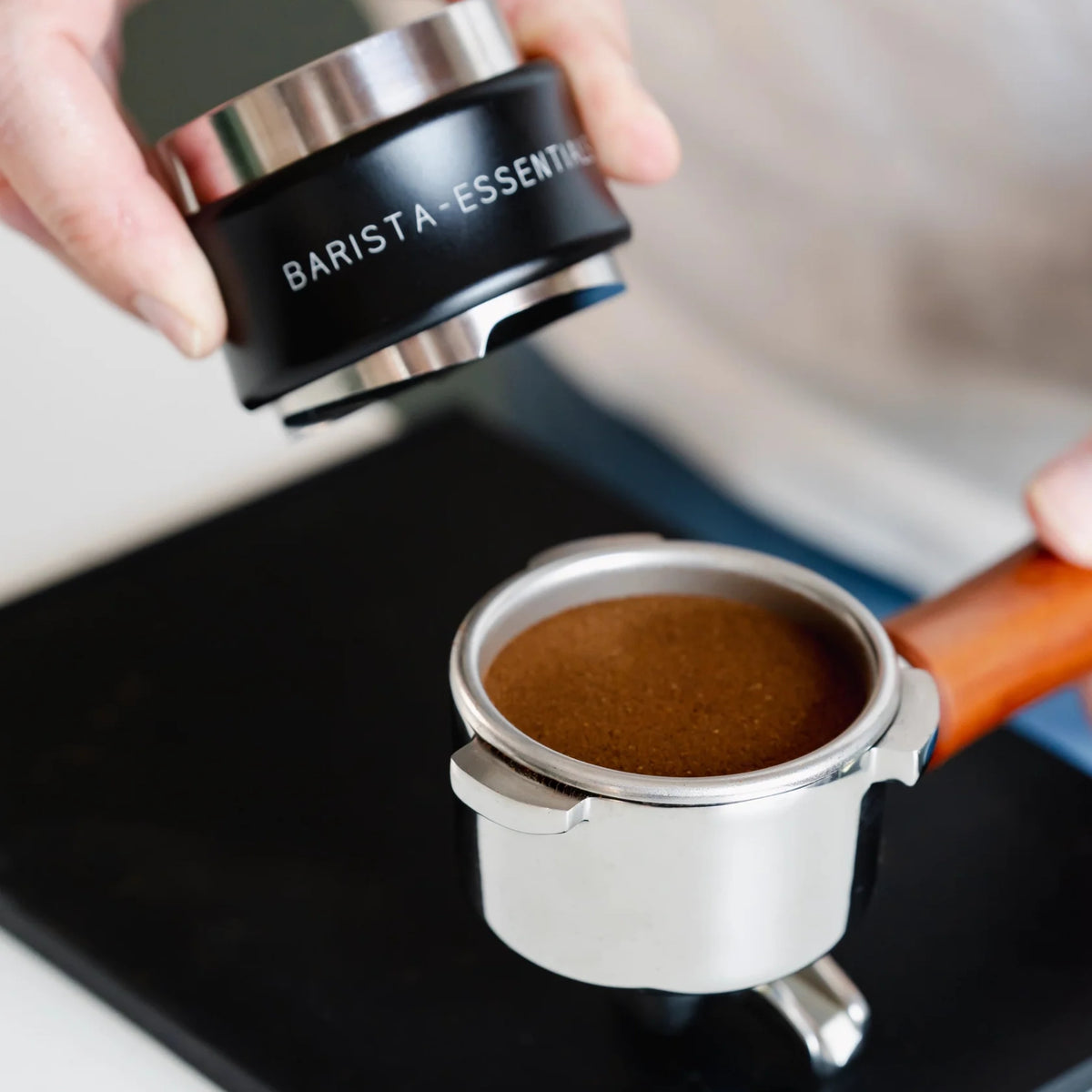 Zwarte koffieverdeler en tamper combinatie boven een portafilter met gemalen koffie