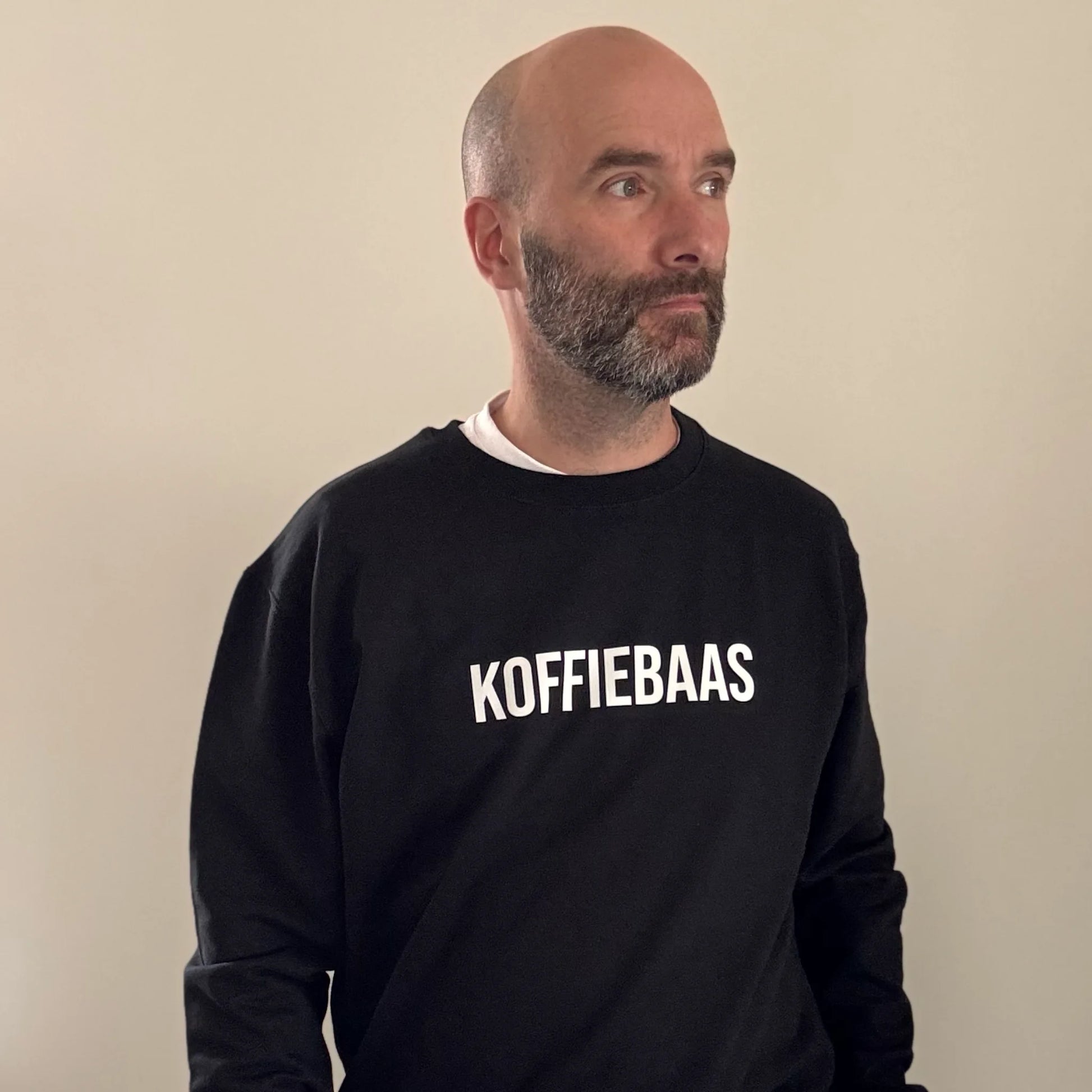 Volledige look van man in zwarte barista sweater met “KOFFIEBAAS” print