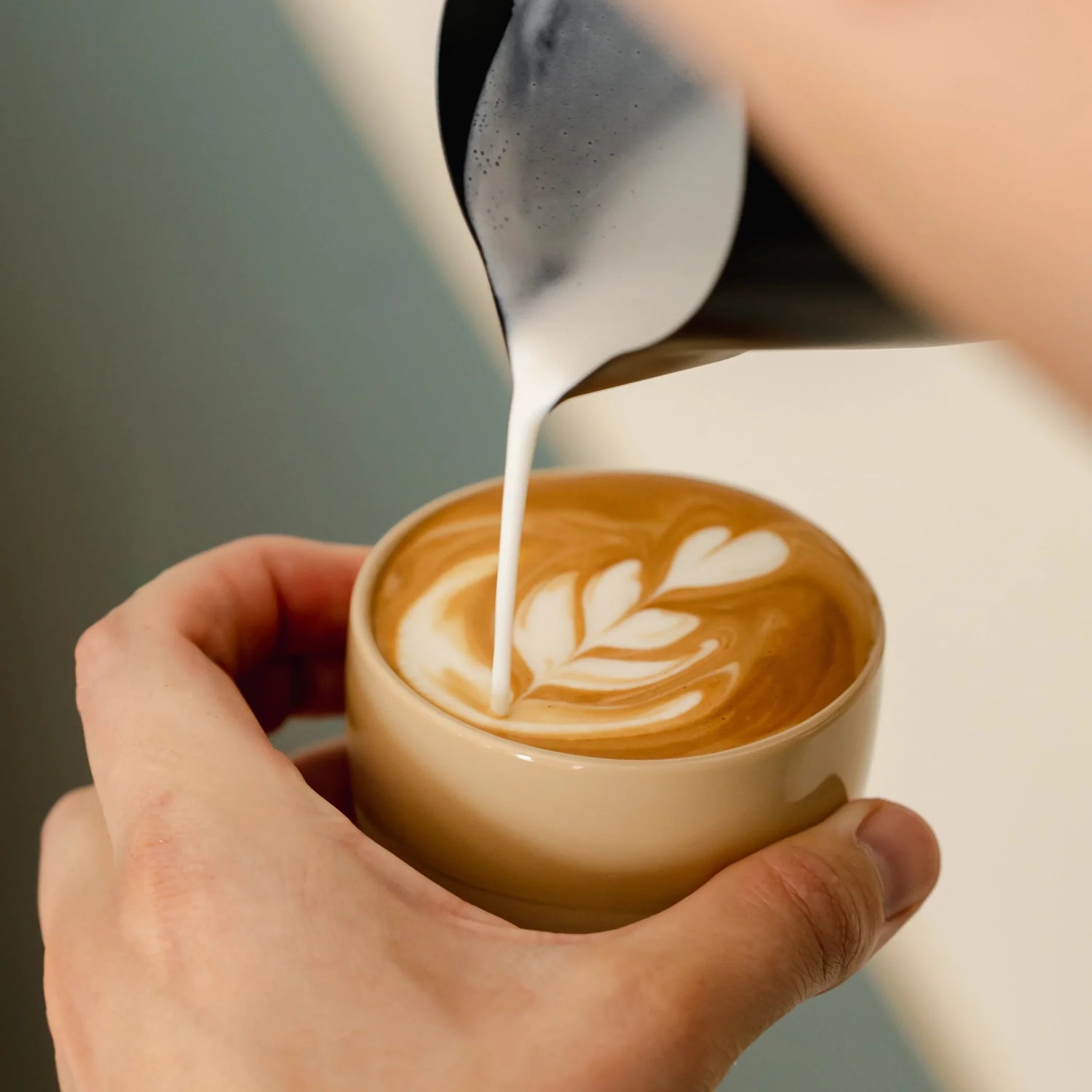 Zandgeel cappuccino kopje van keramiek met latte art, vastgehouden door barista. Ideaal voor thuisgebruik met populaire espressomachines en melkopschuimers.