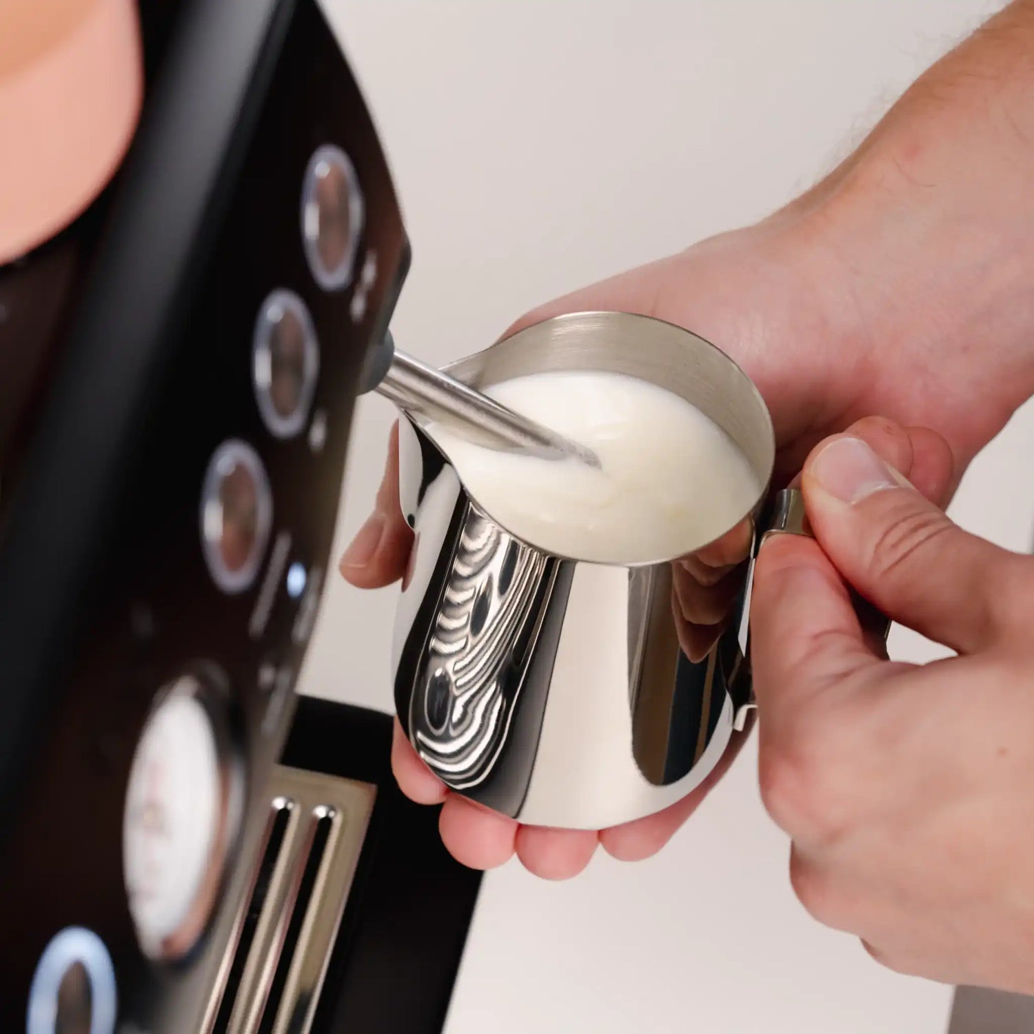 Close-up van thuisbarista die melk opschuimt met een espressomachine en melkkannetje voor zijdezacht microschuim