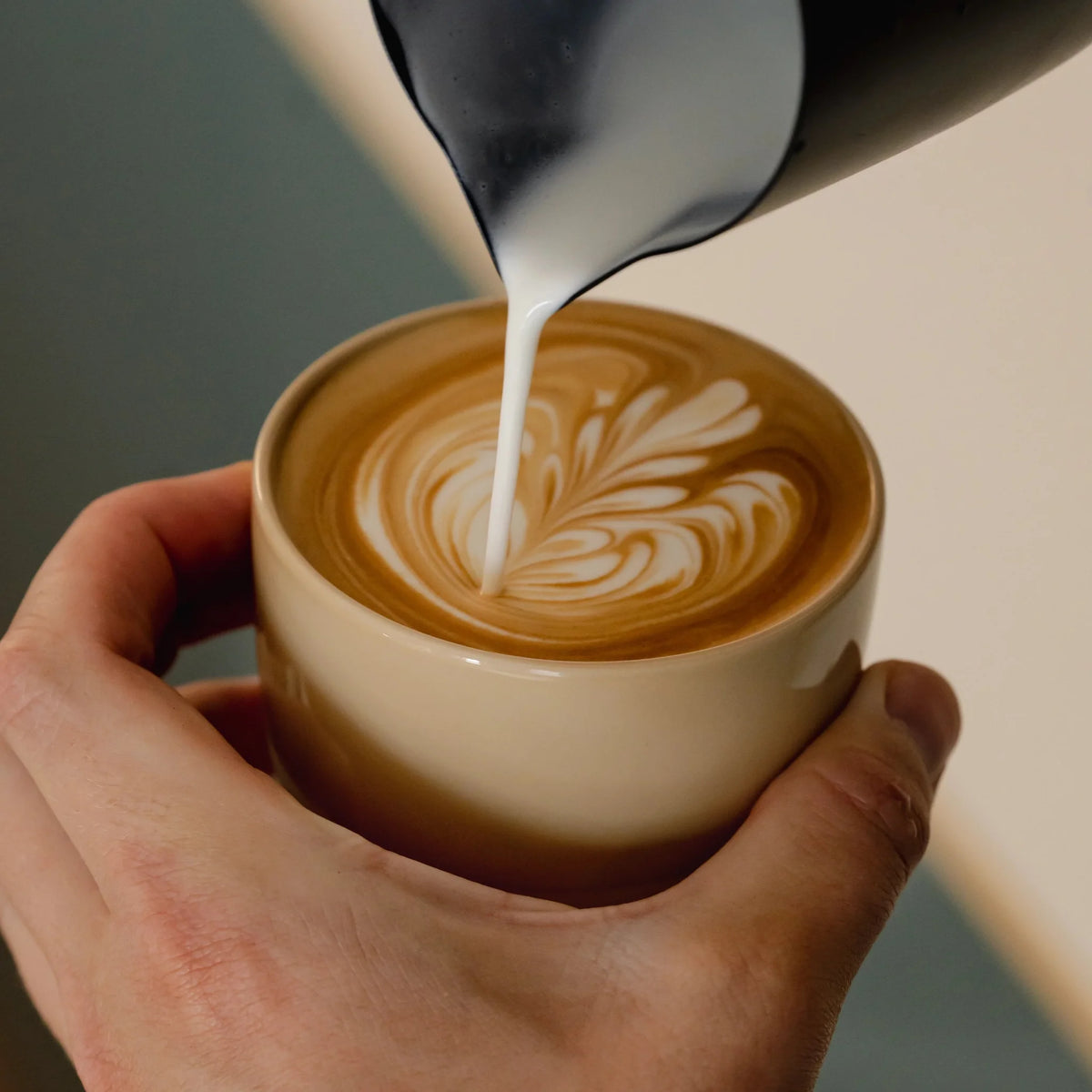 Melk wordt in een zandgeel kopje geschonken voor latte art