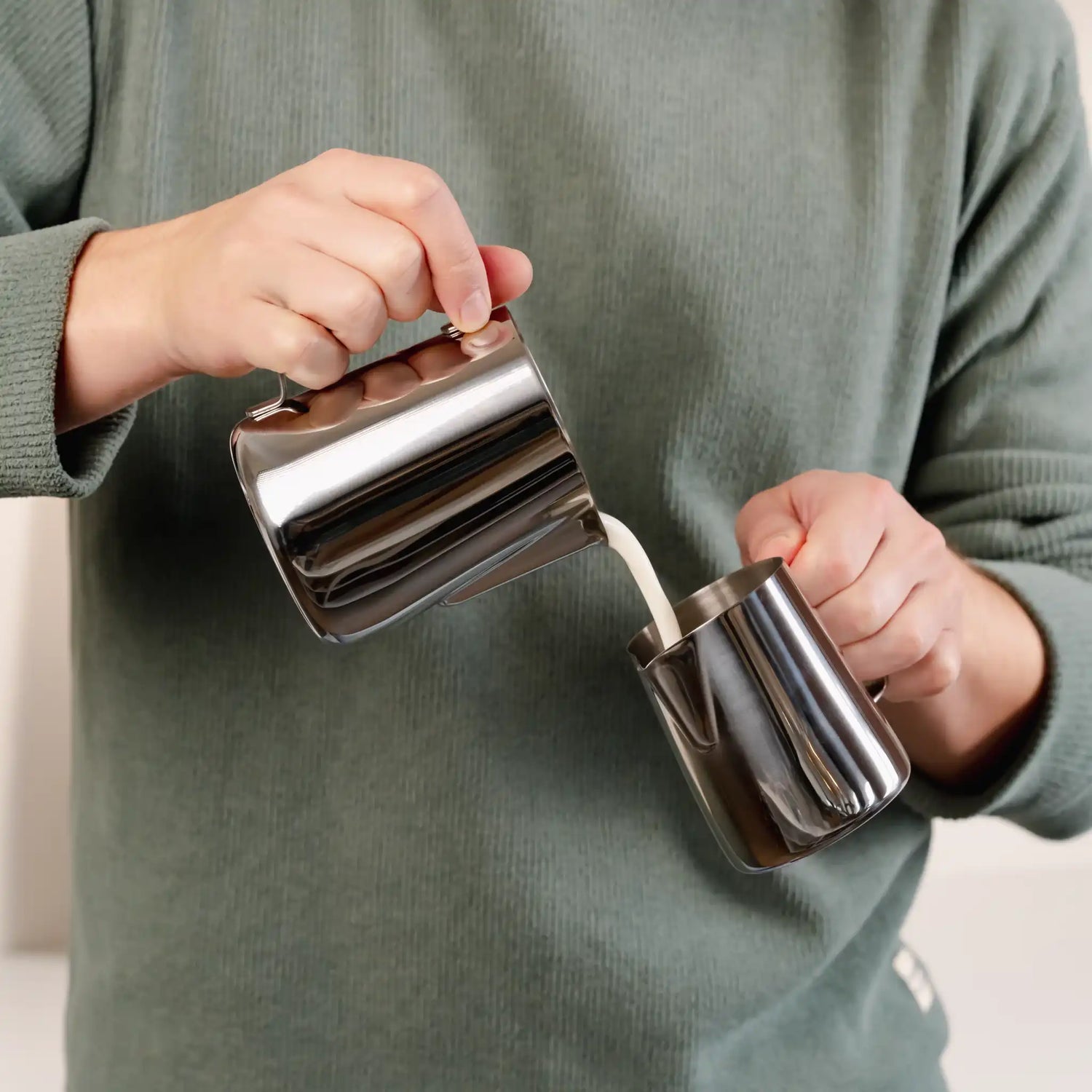 Thuisbarista giet opgeschuimde melk over tussen twee melkkannetjes voor betere textuur en controle bij latte art