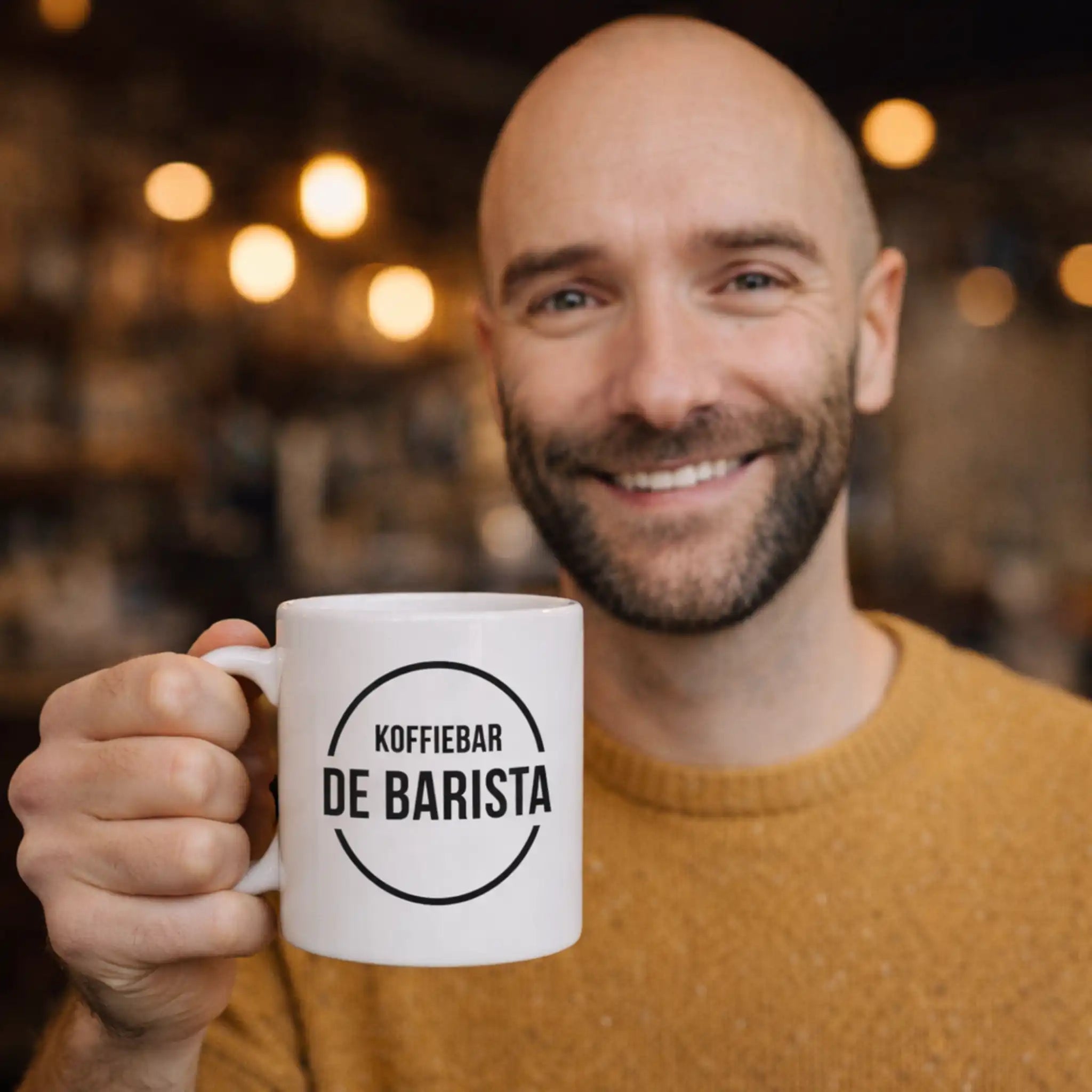 Vriendelijke barista houdt een bedrukte mok vast met het logo van Koffiebar De Barista, gebruikt als gepersonaliseerd servies in de horeca.