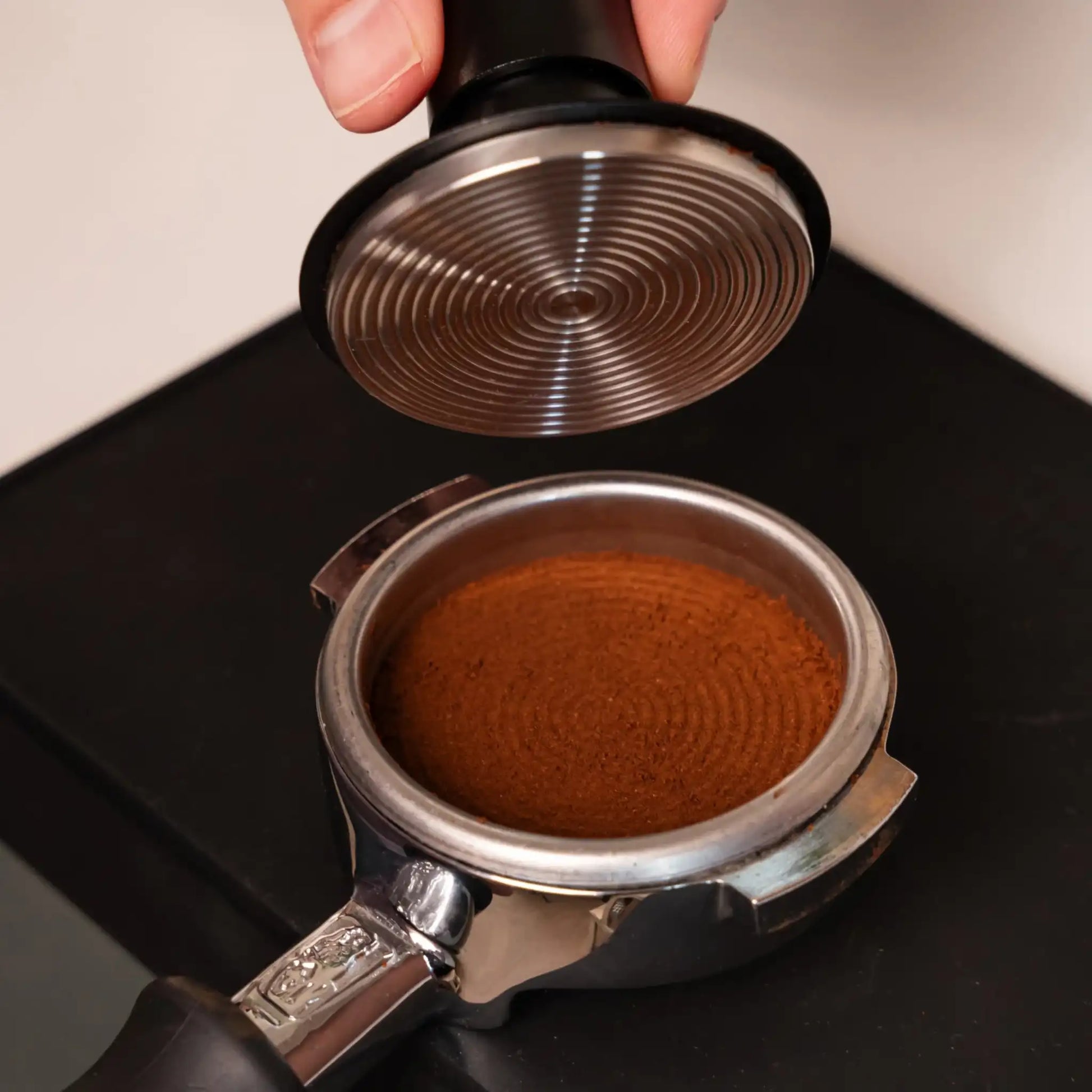 Onderzijde van een gekalibreerde espresso tamper boven een vlak aangedrukte koffiepuck in een portafilter.