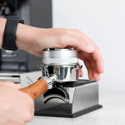 Hand drukt met een tamper koffie aan in een portafilter op het zilveren station