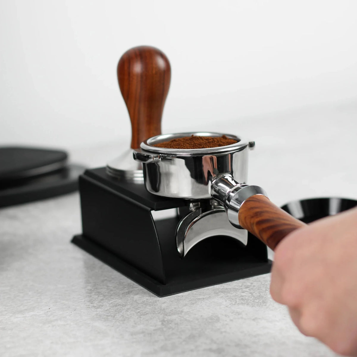 Hand houdt een portafilter met houten handvat op het zwarte tamping station