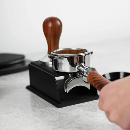 Hand houdt een portafilter met houten handvat op het zwarte tamping station