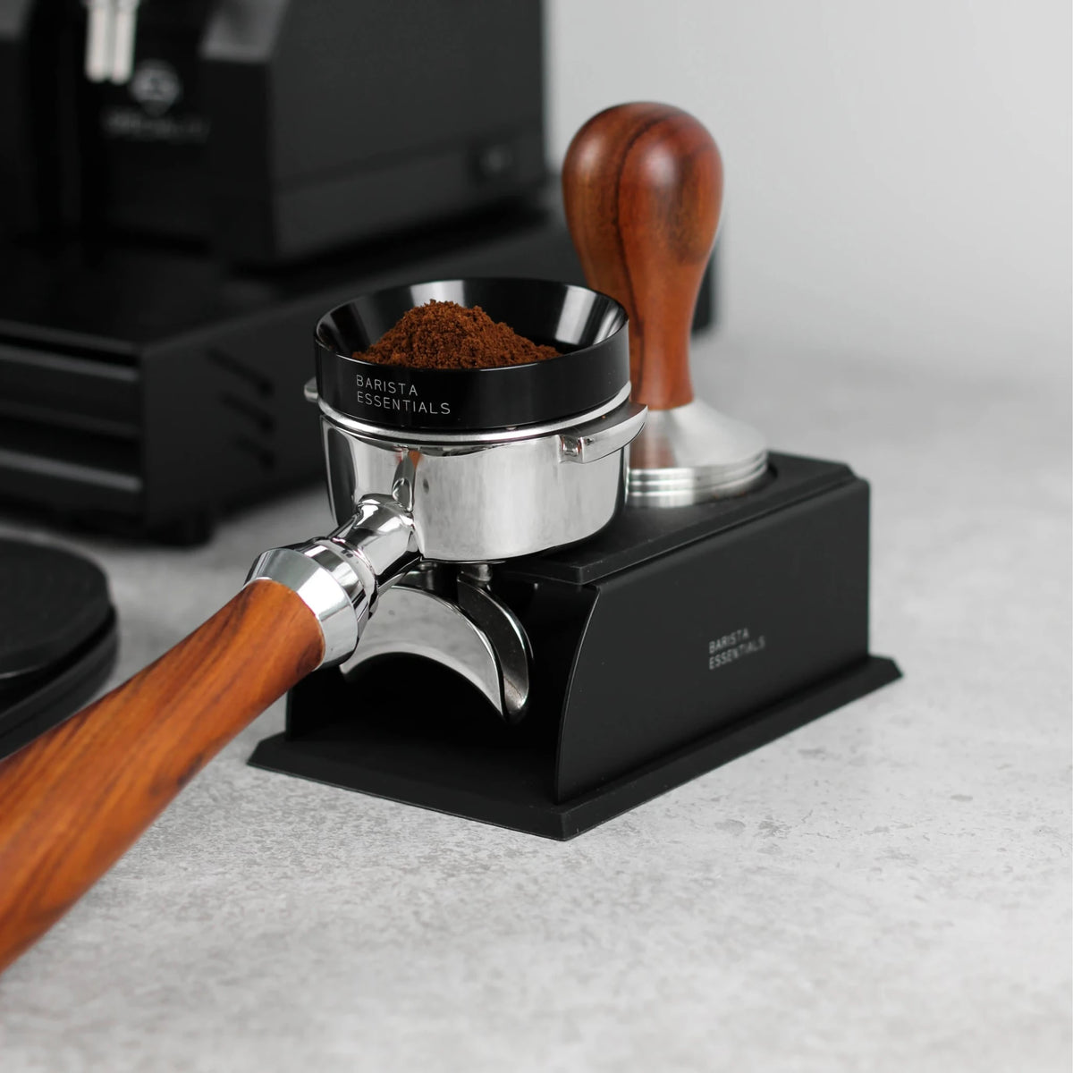 Portafilter en tamper op een zwart tamping station naast een koffiemolen