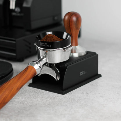 Portafilter en tamper op een zwart tamping station naast een koffiemolen