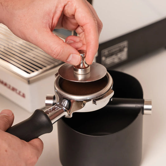 Puck screen 58,5 mm met magneet wordt uit een 58 mm portafilter verwijderd na de espresso-extractie.