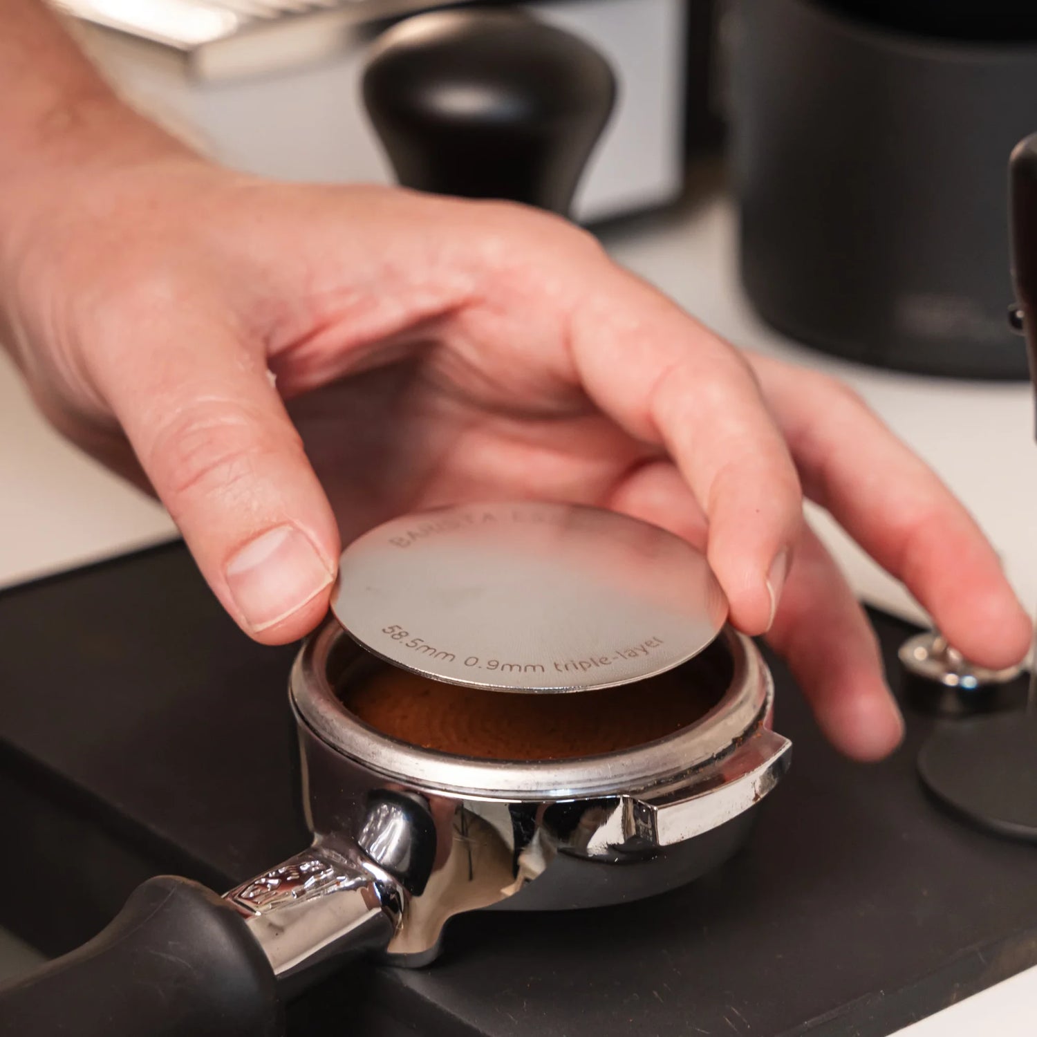 Hand plaatst een 58,5 mm puck screen op een aangetampte koffiepuck in een 58 mm E61-portafilter.