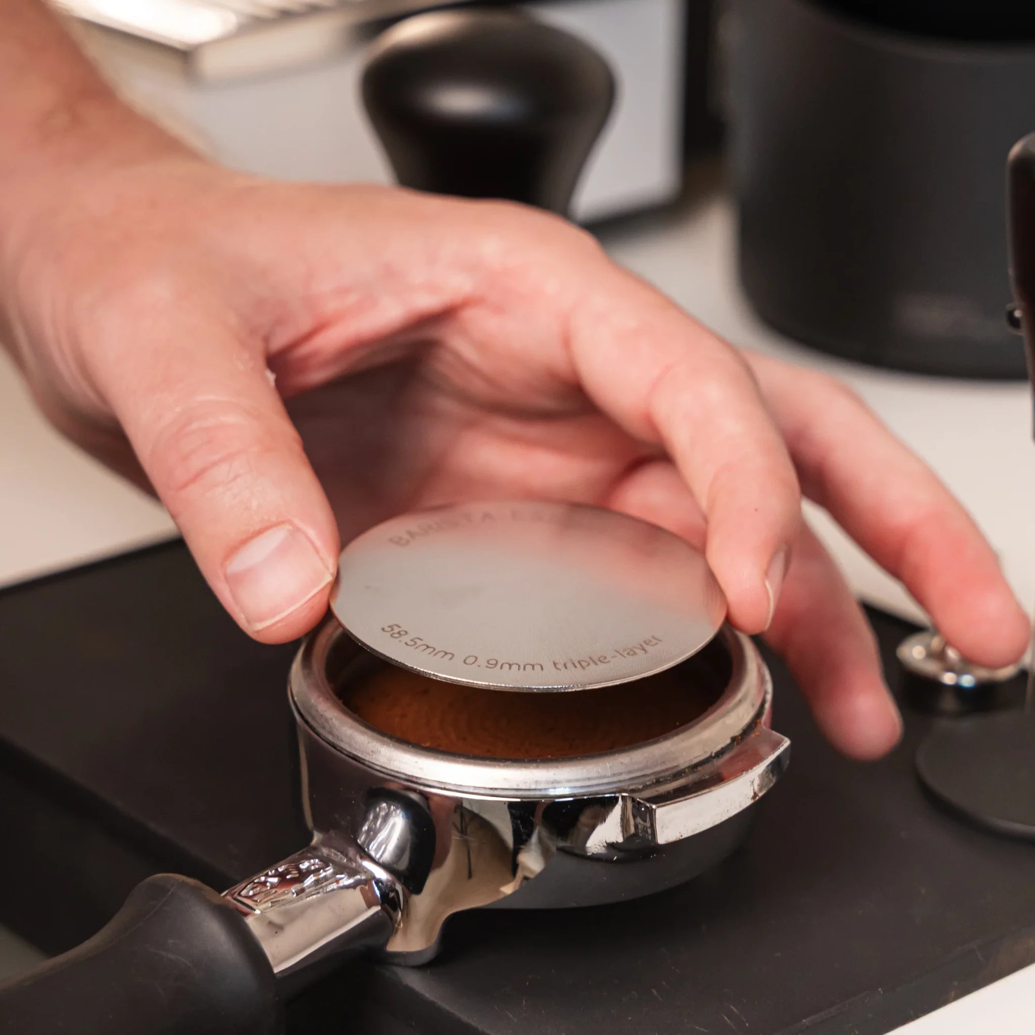 Hand plaatst een 58,5 mm puck screen op een aangetampte koffiepuck in een 58 mm E61-portafilter.