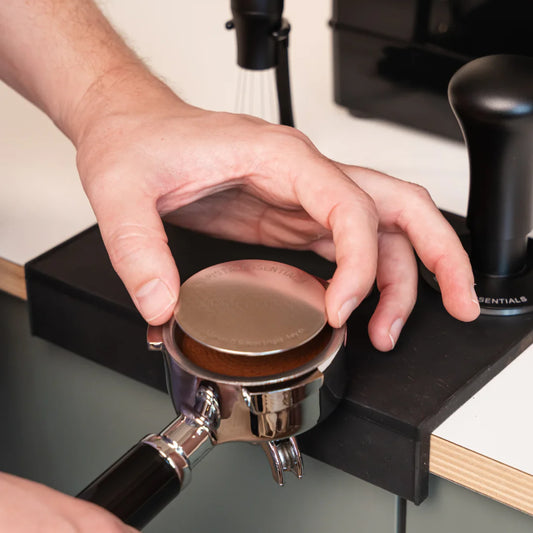 Puck Screen V2 58 mm wordt op een getampte koffiepuck in een Quick Mill portafilter geplaatst voor een rustigere waterverdeling.