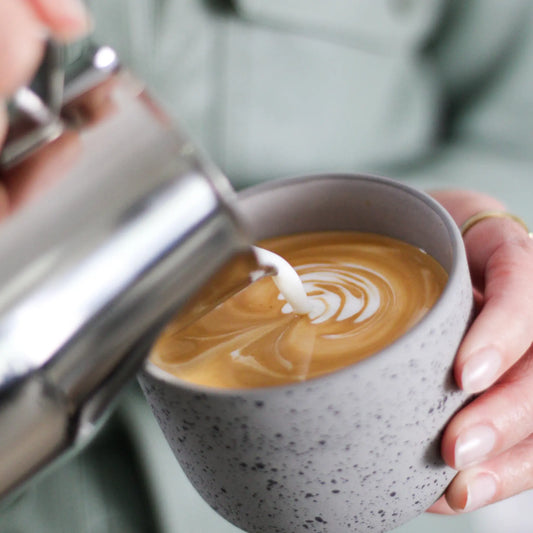 Hand schenkt melk vanuit een RVS kan in een kop cappuccino